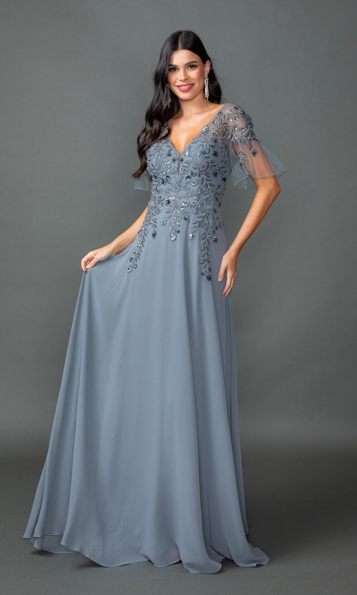 A woman poses in front of a gray background, wearing the Dancing Queen 4378 Sheer Short-Sleeve Prom Dress in dark silver, featuring beaded details and sheer embroidered sleeves.